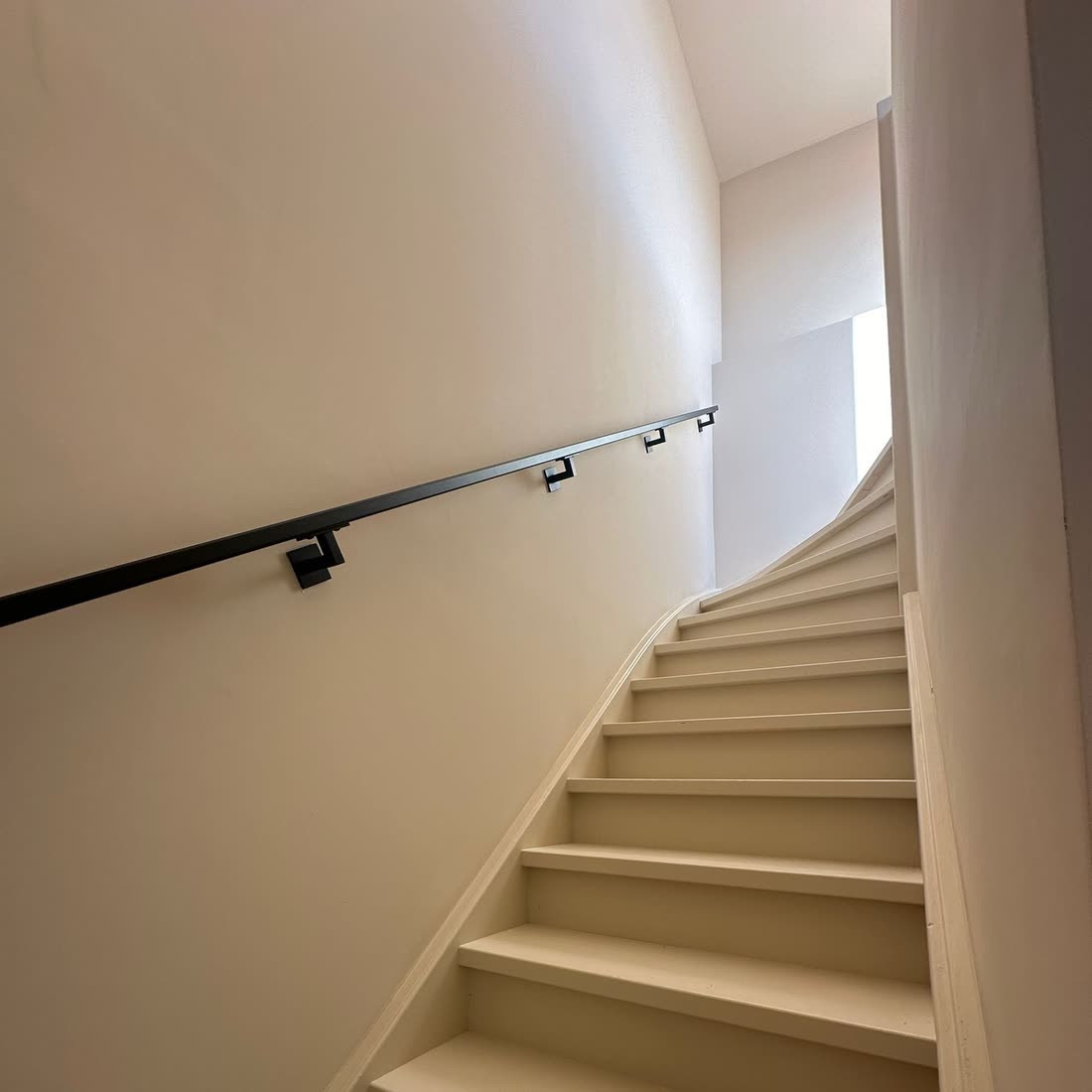 Bestaande trap opnieuw afgewerkt, met een stalen leuning strak langs de gestucte wand